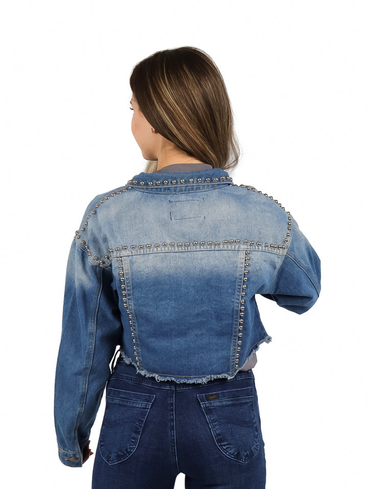 Mujer vistiendo una chamarra corta de mezclilla color azul claro con detalles de remaches plateados.