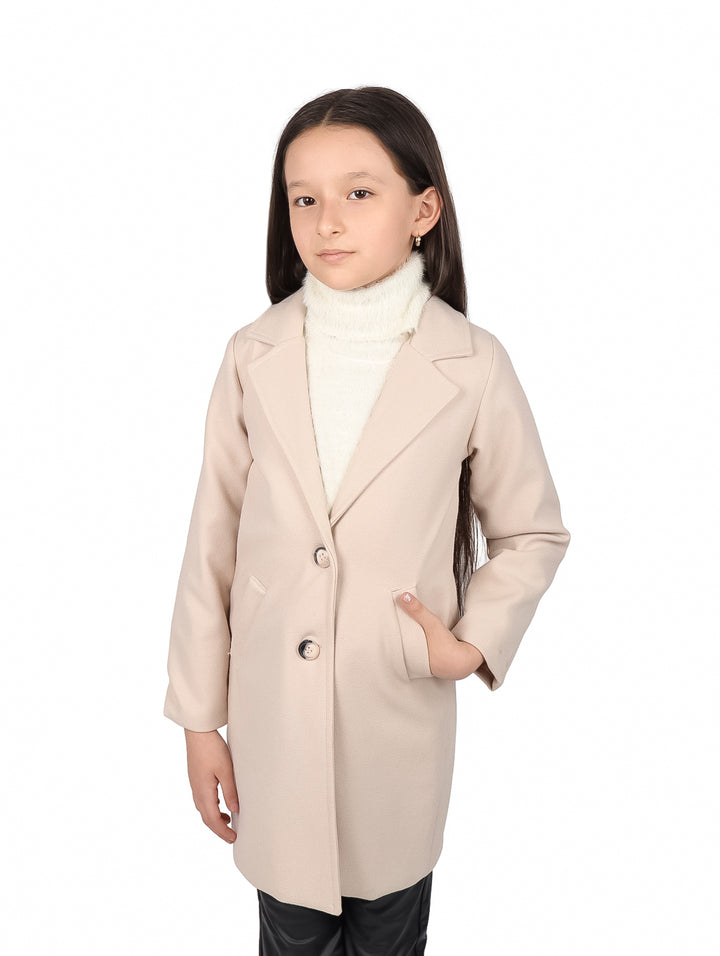 Niña vistiendo un abrigo beige elegante con botones y solapas sobre un suéter blanco.
