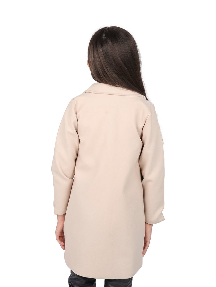 Niña vistiendo un abrigo beige elegante con botones y solapas sobre un suéter blanco.