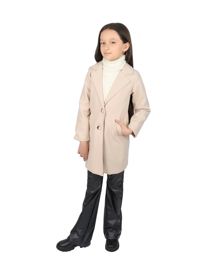 Niña vistiendo un abrigo beige elegante con botones y solapas sobre un suéter blanco.