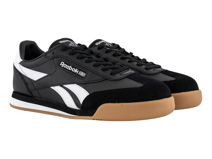 Tenis Reebok negros con franjas blancas y suela de goma color miel.