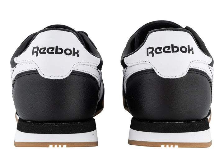 Tenis Reebok negros con franjas blancas y suela de goma color miel.