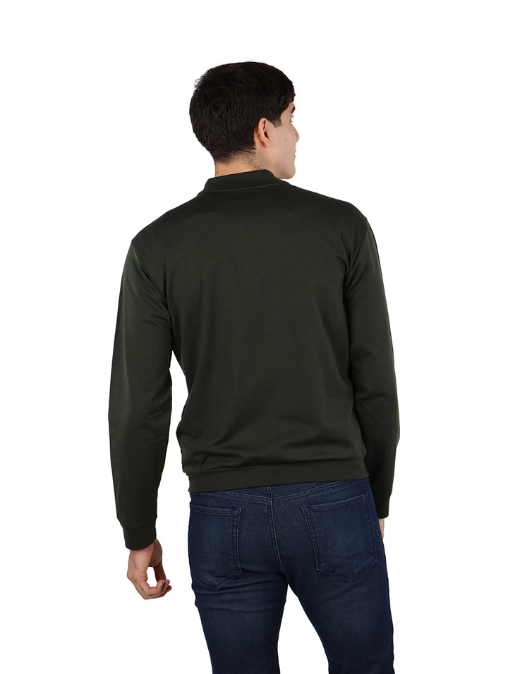 Hombre vistiendo una chamarra bomber color verde militar con cierre frontal y pantalones azul marino.