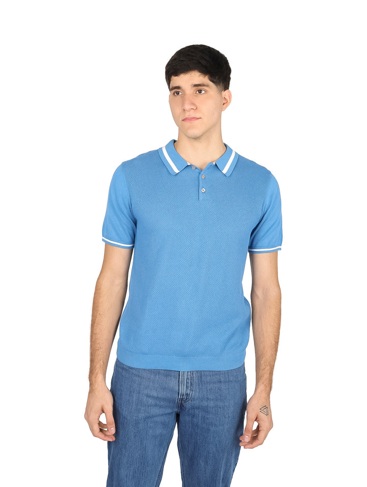 Hombre vistiendo una playera polo color azul claro con ribetes blancos en el cuello y las mangas.