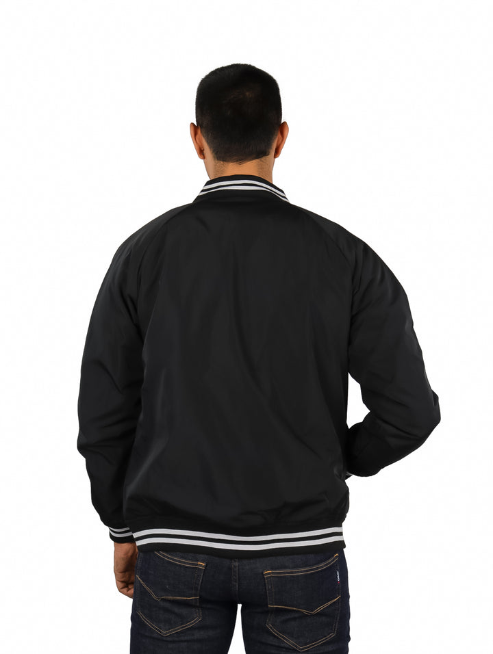 Hombre vistiendo una chamarra bomber negra de K-SWISS con detalles blancos en cuello y puños.