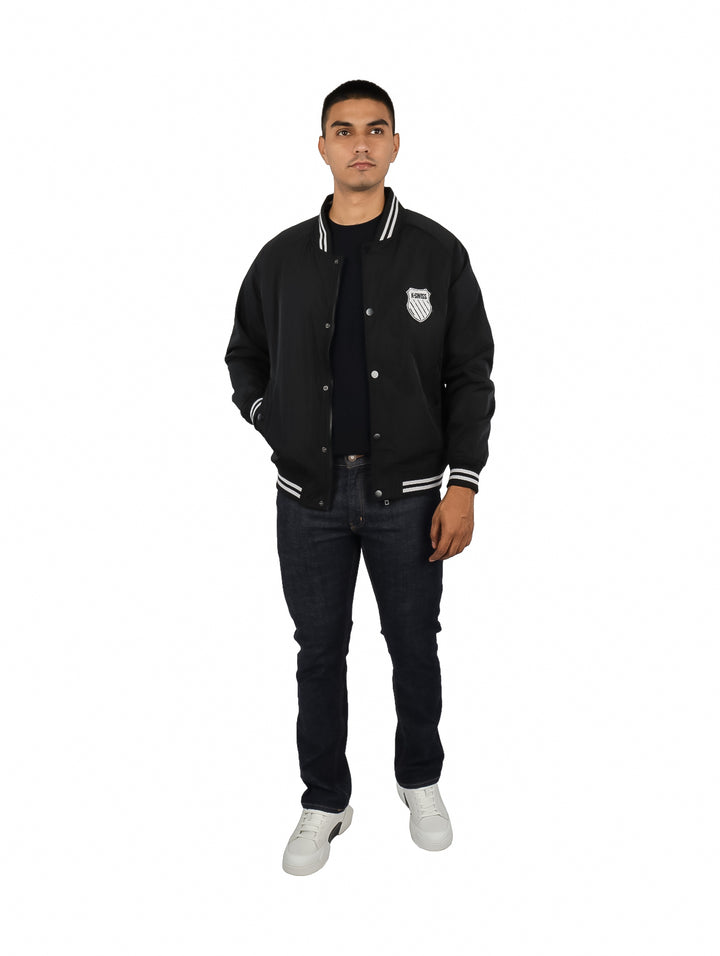 Hombre vistiendo una chamarra bomber negra de K-SWISS con detalles blancos en cuello y puños.