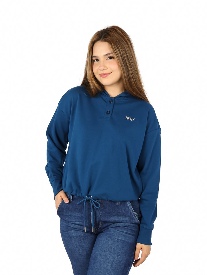 Mujer vistiendo una sudadera azul DKNY con capucha y pantalones de mezclilla.
