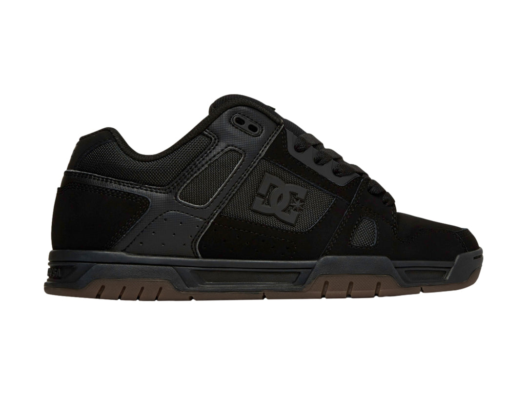 Tenis DC Shoes color negro con suela de goma marrón, diseño deportivo para skate.