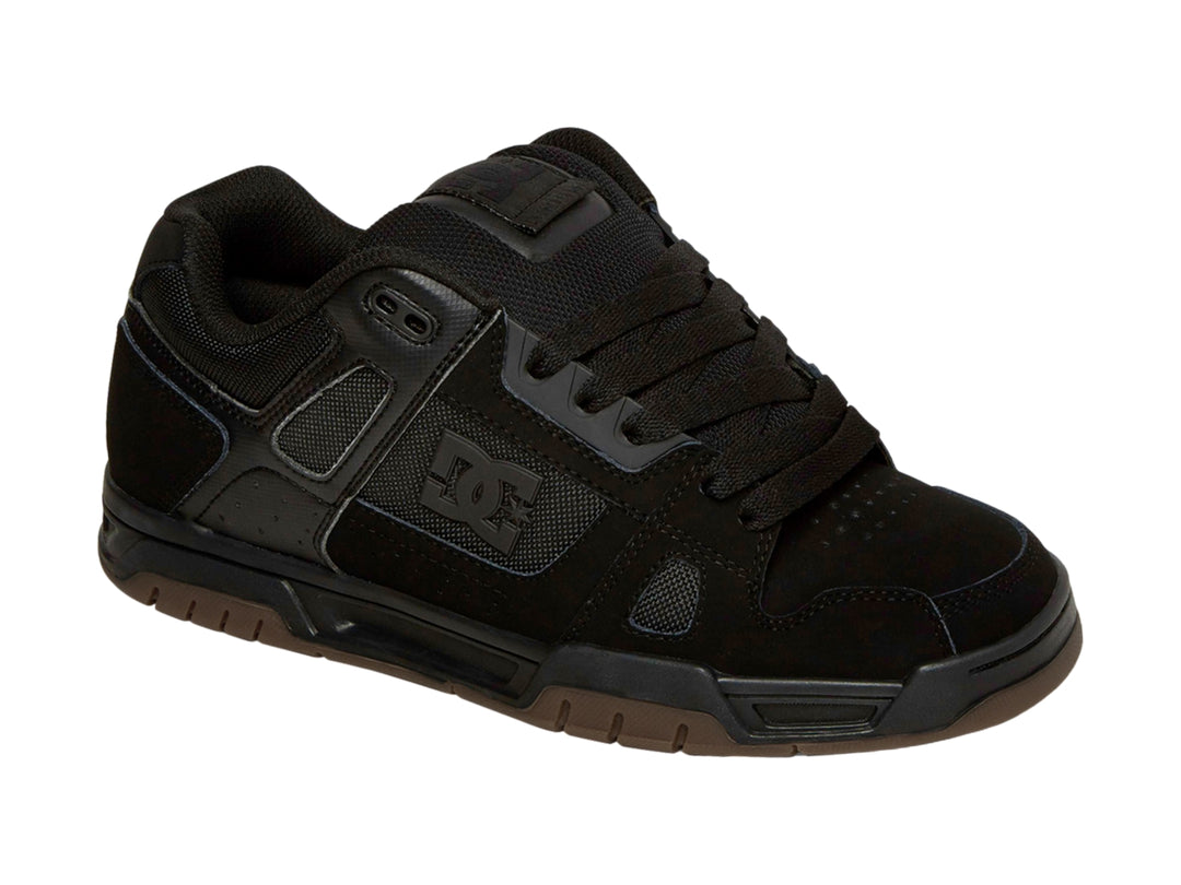 Tenis DC Shoes color negro con suela de goma marrón, diseño deportivo para skate.