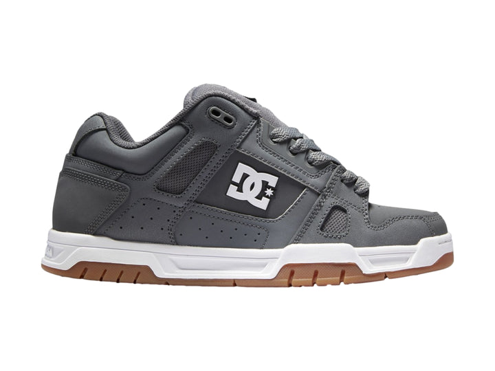 Tenis DC Shoes color gris con suela blanca y marrón, diseño deportivo de corte bajo.