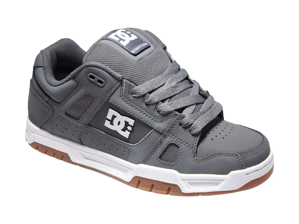 Tenis DC Shoes color gris con suela blanca y marrón, diseño deportivo de corte bajo.
