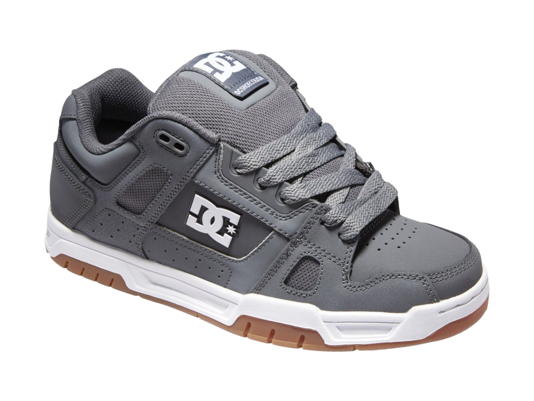 Tenis DC Shoes color gris con suela blanca y marrón, diseño deportivo de corte bajo.