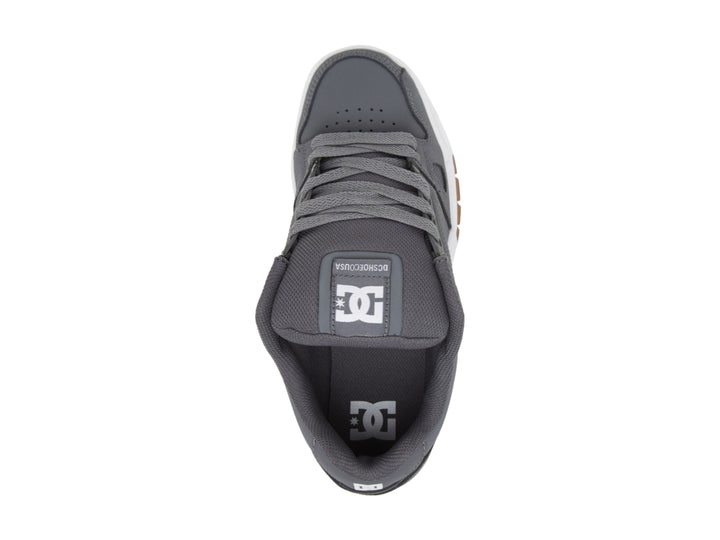 Tenis DC Shoes color gris con suela blanca y marrón, diseño deportivo de corte bajo.