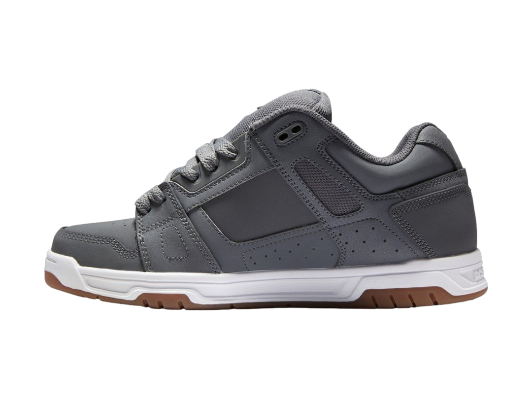 Tenis DC Shoes color gris con suela blanca y marrón, diseño deportivo de corte bajo.