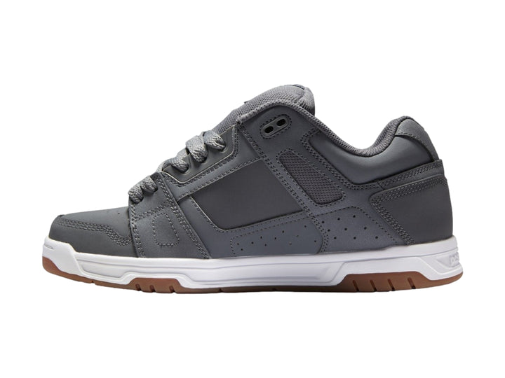 Tenis DC Shoes color gris con suela blanca y marrón, diseño deportivo de corte bajo.