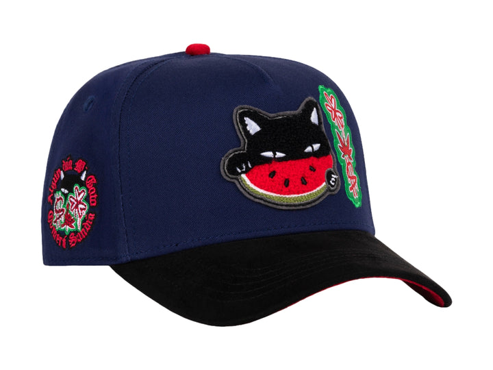 Gorra snapback azul con visera negra y parches decorativos de gato sandía y diseño floral.