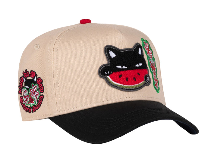 Gorra snapback color beige con visera negra, decorada con un parche de gato comiendo sandía y detalles en rojo.