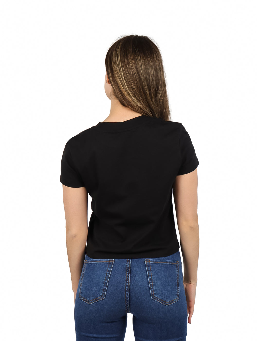 Mujer vistiendo blusa negra de manga corta con logotipo de Calvin Klein y jeans azules.