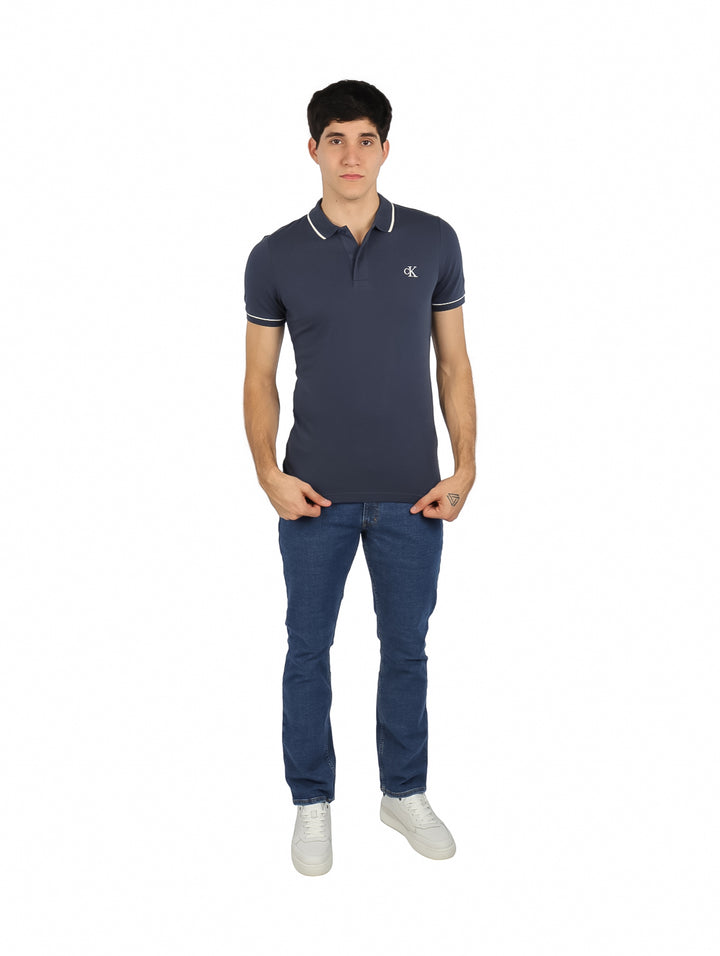 Hombre vistiendo una camiseta polo azul marino de Calvin Klein con detalles blancos en el cuello y mangas.