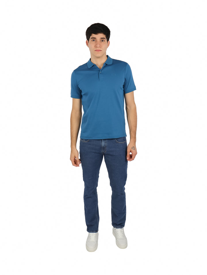 Hombre vistiendo una playera polo azul de manga corta de la marca Calvin Klein.