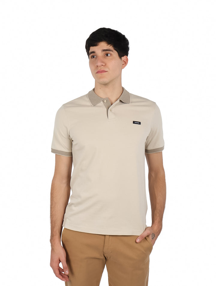 Hombre vistiendo playera polo color beige de Calvin Klein con pantalones color café claro.
