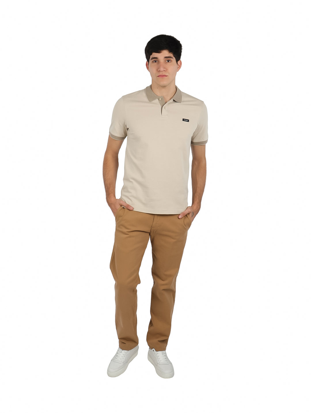 Hombre vistiendo playera polo color beige de Calvin Klein con pantalones color café claro.