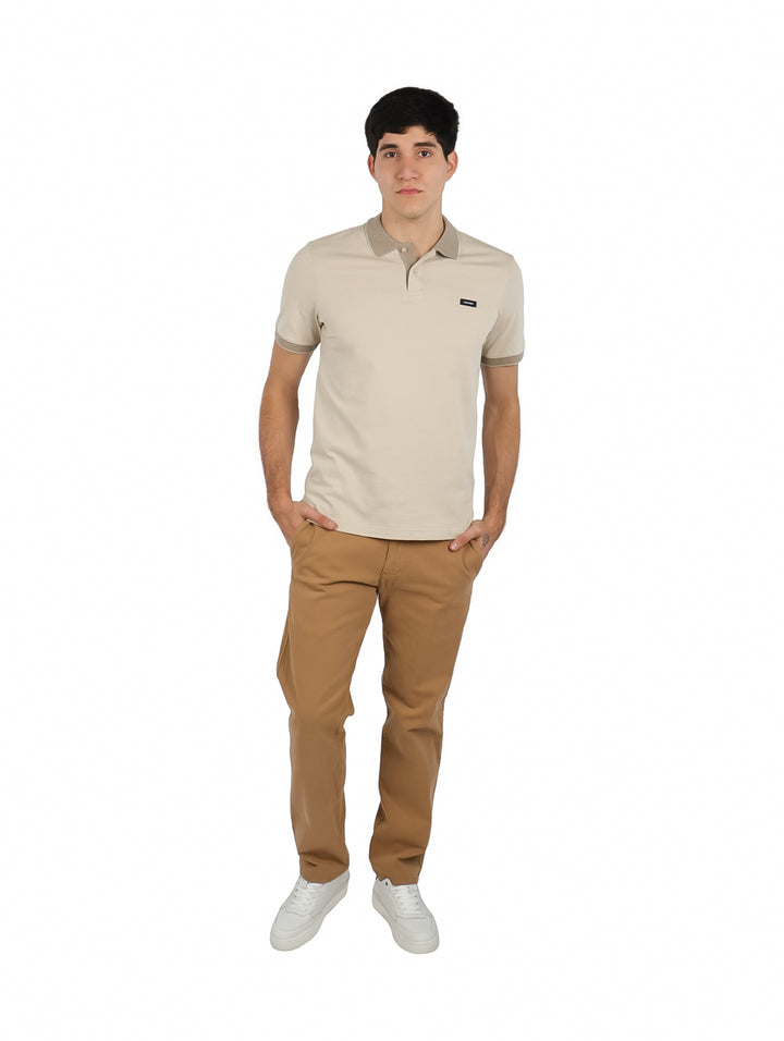 Hombre vistiendo playera polo color beige de Calvin Klein con pantalones color café claro.