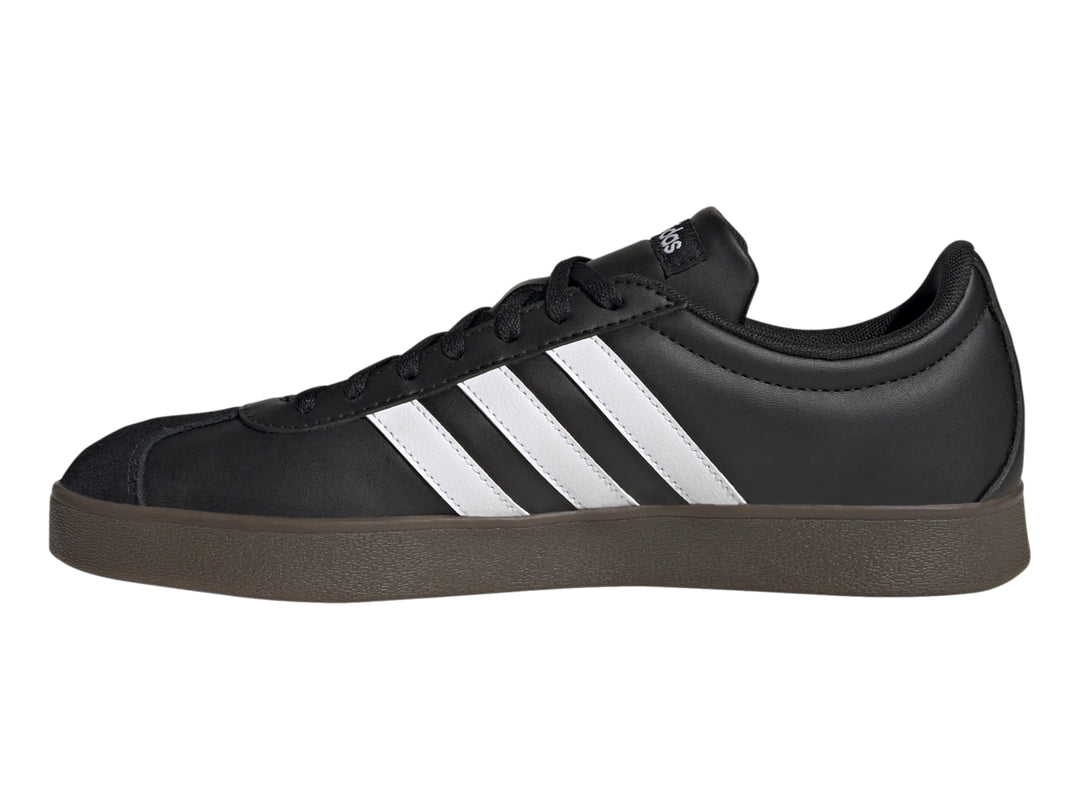 Tenis Adidas color negro con tres franjas blancas laterales y suela marrón oscuro.