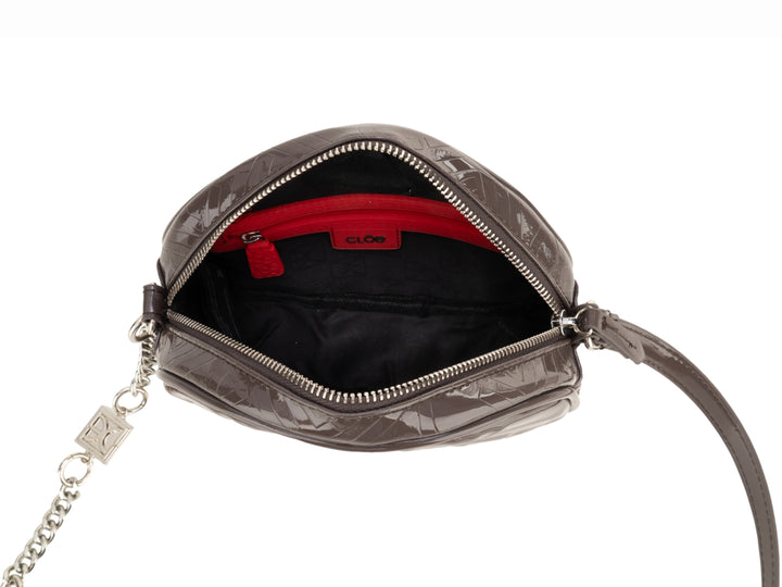 Bolso circular Cloe en color gris con acabado brillante, correa larga y detalles de cadena plateada.