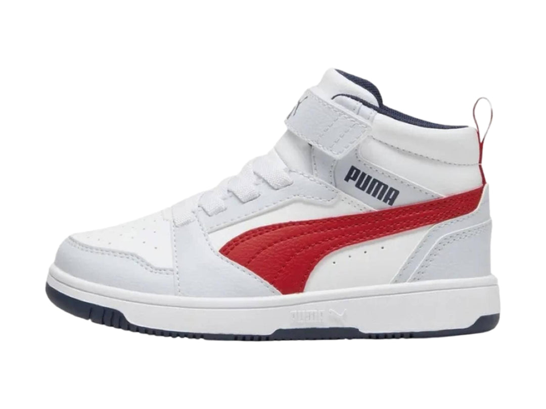 Tenis PUMA blancos de corte medio con franja roja lateral y suela azul marino.