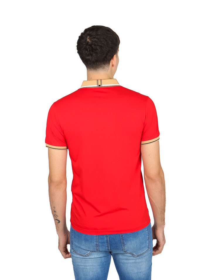 Hombre vistiendo playera polo color rojo con detalles en beige en el cuello y mangas, combinada con jeans azules.