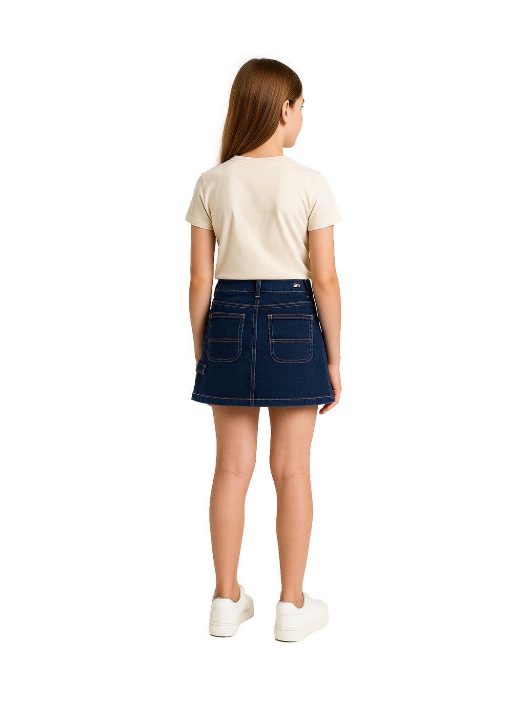 Niña vistiendo una falda corta de mezclilla azul oscuro estilo cargo con camiseta beige y tenis blancos.