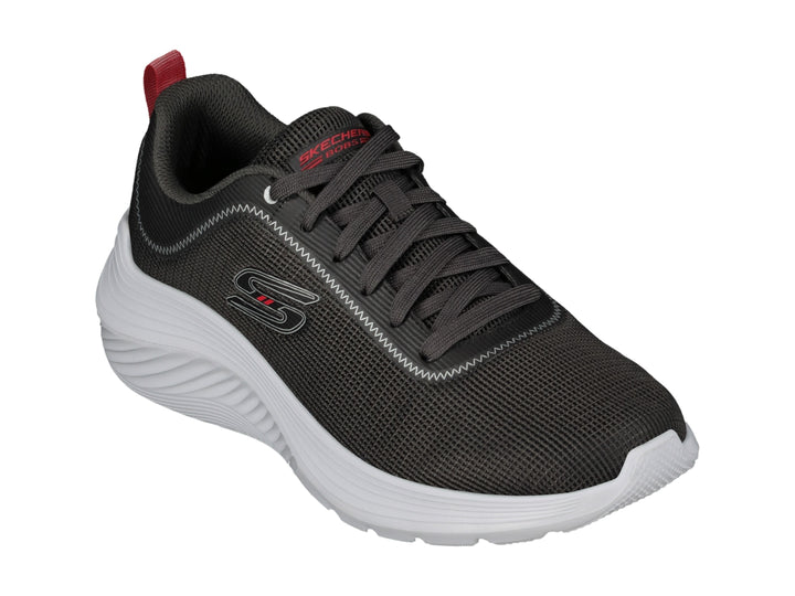 Tenis deportivos Skechers color gris con suela blanca y pequeña pestaña roja en el talón.