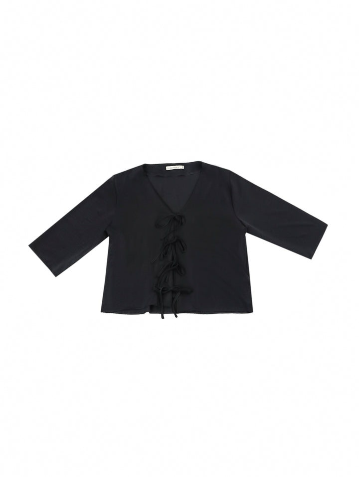 Mujer vistiendo blusa negra con escote en V y detalles de cordones frontales.