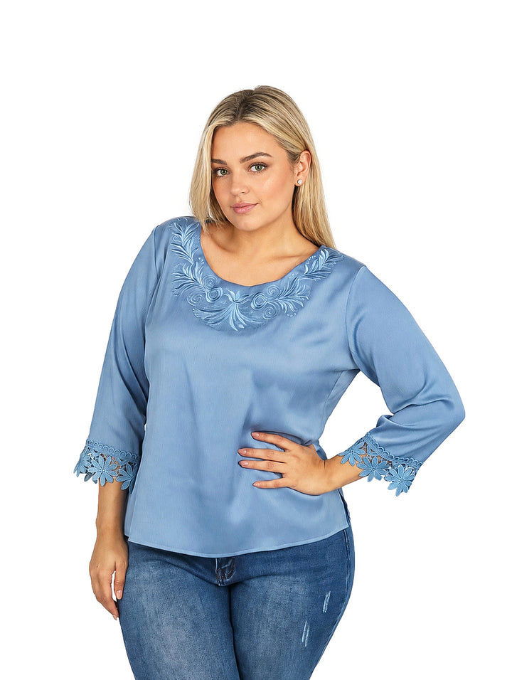 Mujer vistiendo blusa azul de manga 3/4 con detalles de guipure en el cuello y puños.