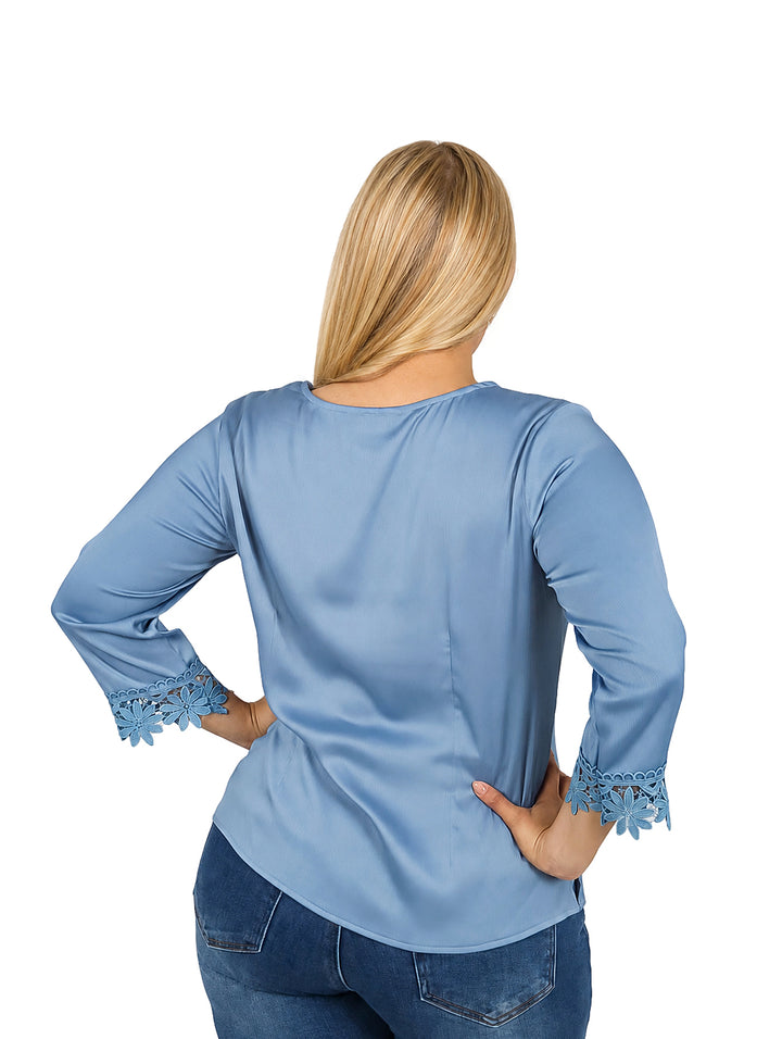Mujer vistiendo blusa azul de manga 3/4 con detalles de guipure en el cuello y puños.