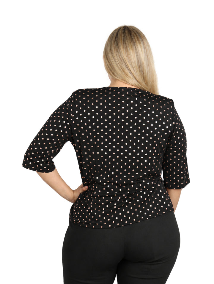 Mujer vistiendo blusa negra con lunares dorados y cuello drapeado.