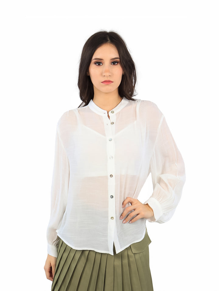 Mujer vistiendo una blusa blanca de manga larga con botones y falda verde plisada.