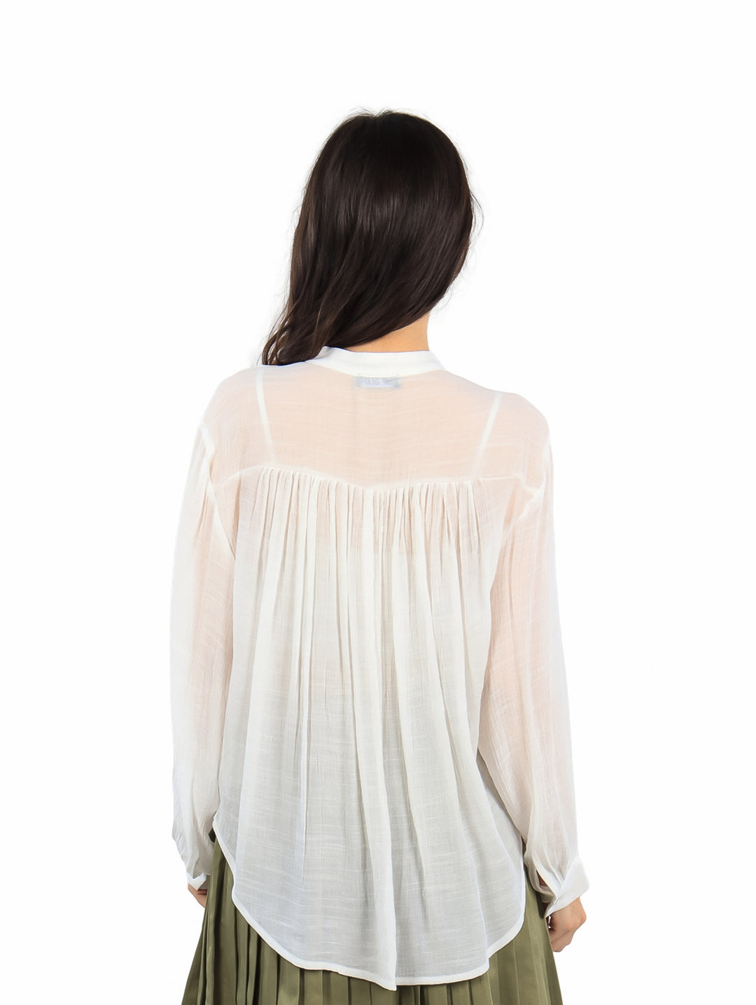 Mujer vistiendo una blusa blanca de manga larga con botones y falda verde plisada.