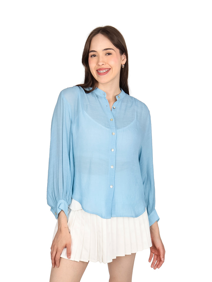 Mujer vistiendo una camisa de botones color azul claro y falda blanca plisada.