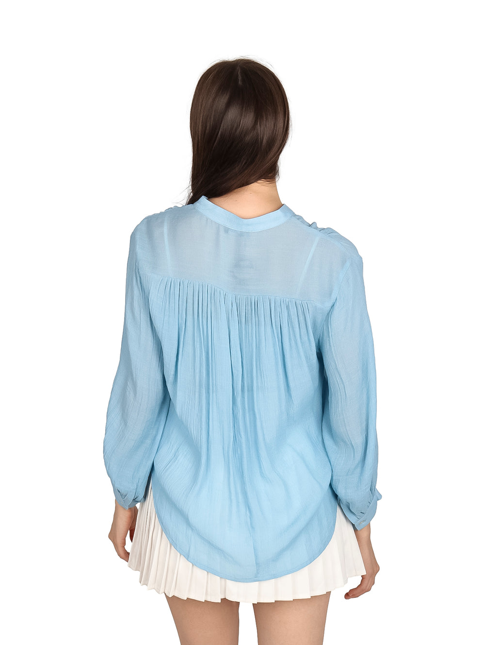Mujer vistiendo una camisa de botones color azul claro y falda blanca plisada.
