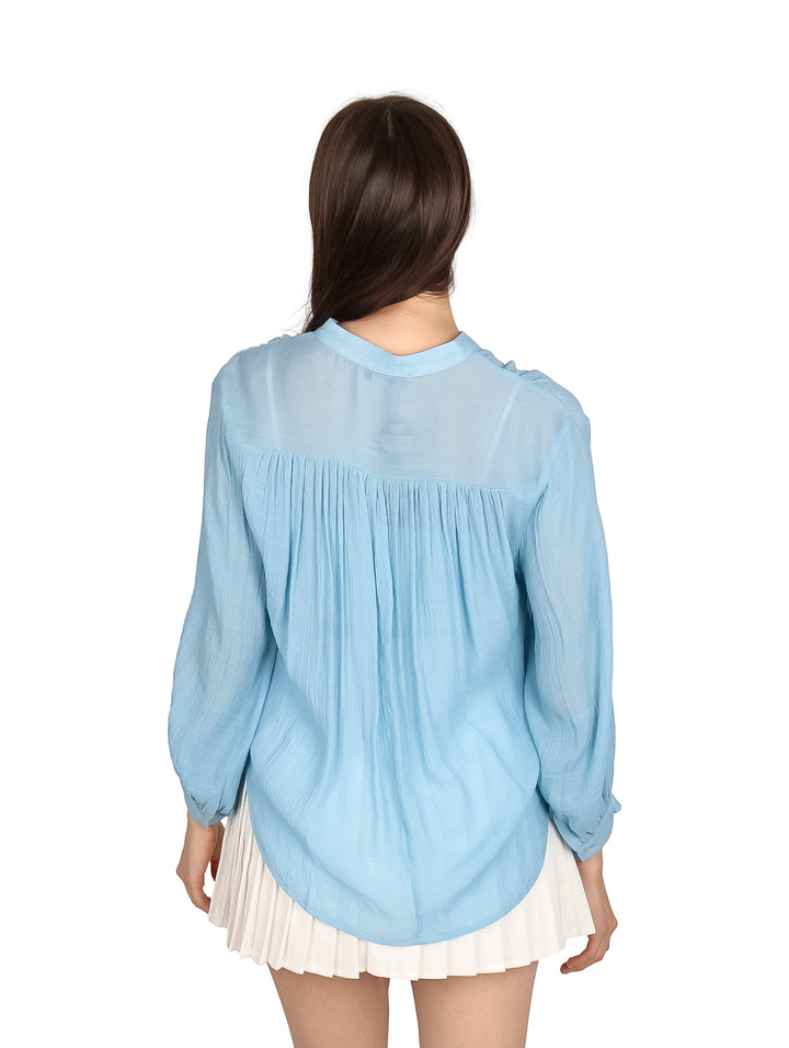 Mujer vistiendo una camisa de botones color azul claro y falda blanca plisada.