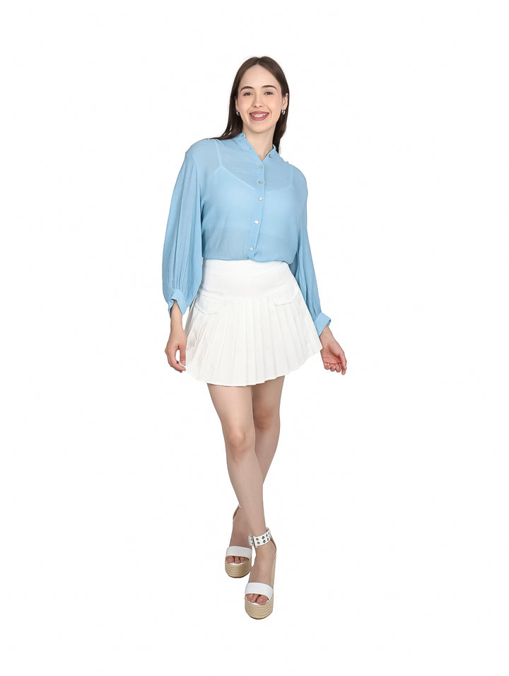Mujer vistiendo una camisa de botones color azul claro y falda blanca plisada.