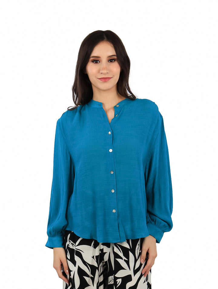Mujer vistiendo una camisa azul de manga larga con botones frontales y corte holgado.