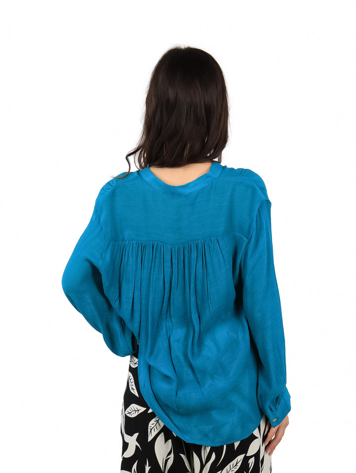 Mujer vistiendo una camisa azul de manga larga con botones frontales y corte holgado.