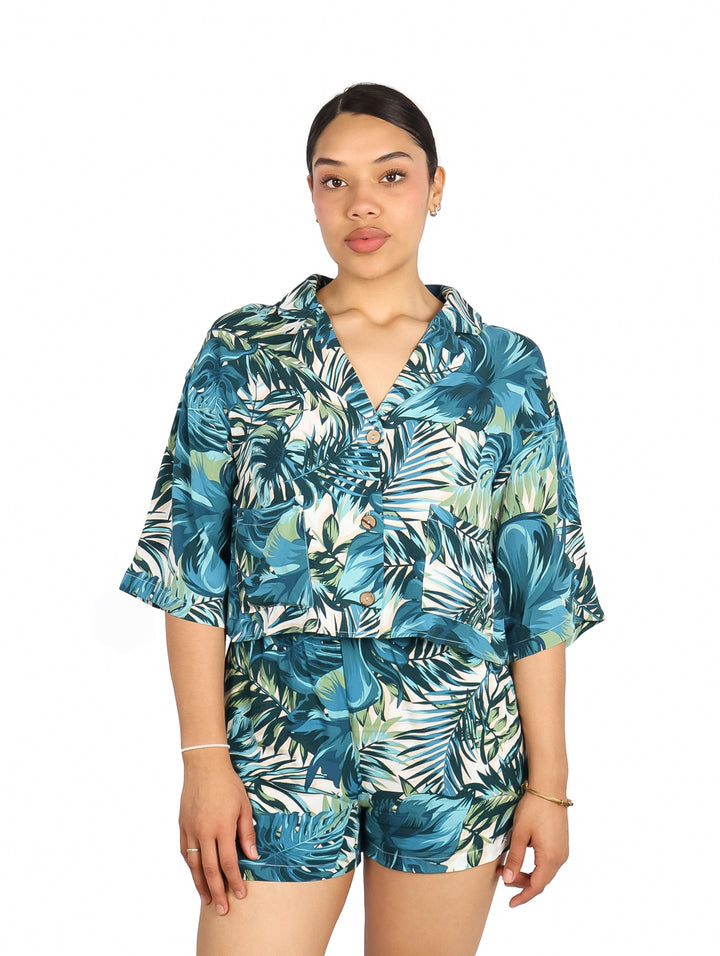Mujer vistiendo blusa y shorts con estampado tropical en tonos verdes y azules.