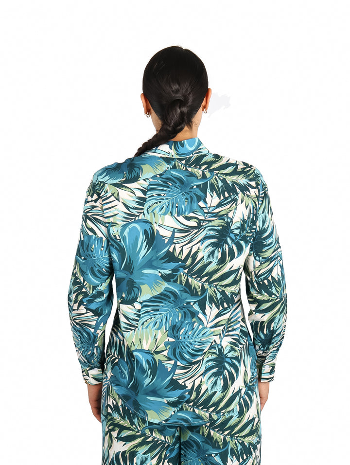 Mujer vistiendo camisa de manga larga con estampado de hojas tropicales en tonos verdes y azules.