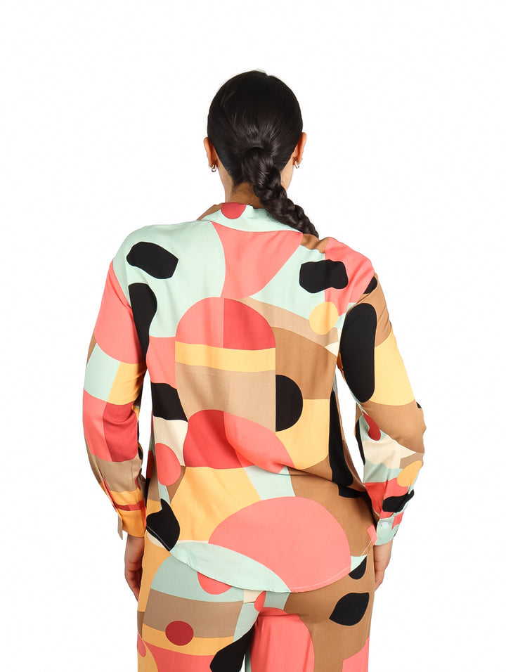 Mujer vistiendo camisa de manga larga con estampado geométrico multicolor en tonos marrón, verde menta y coral.