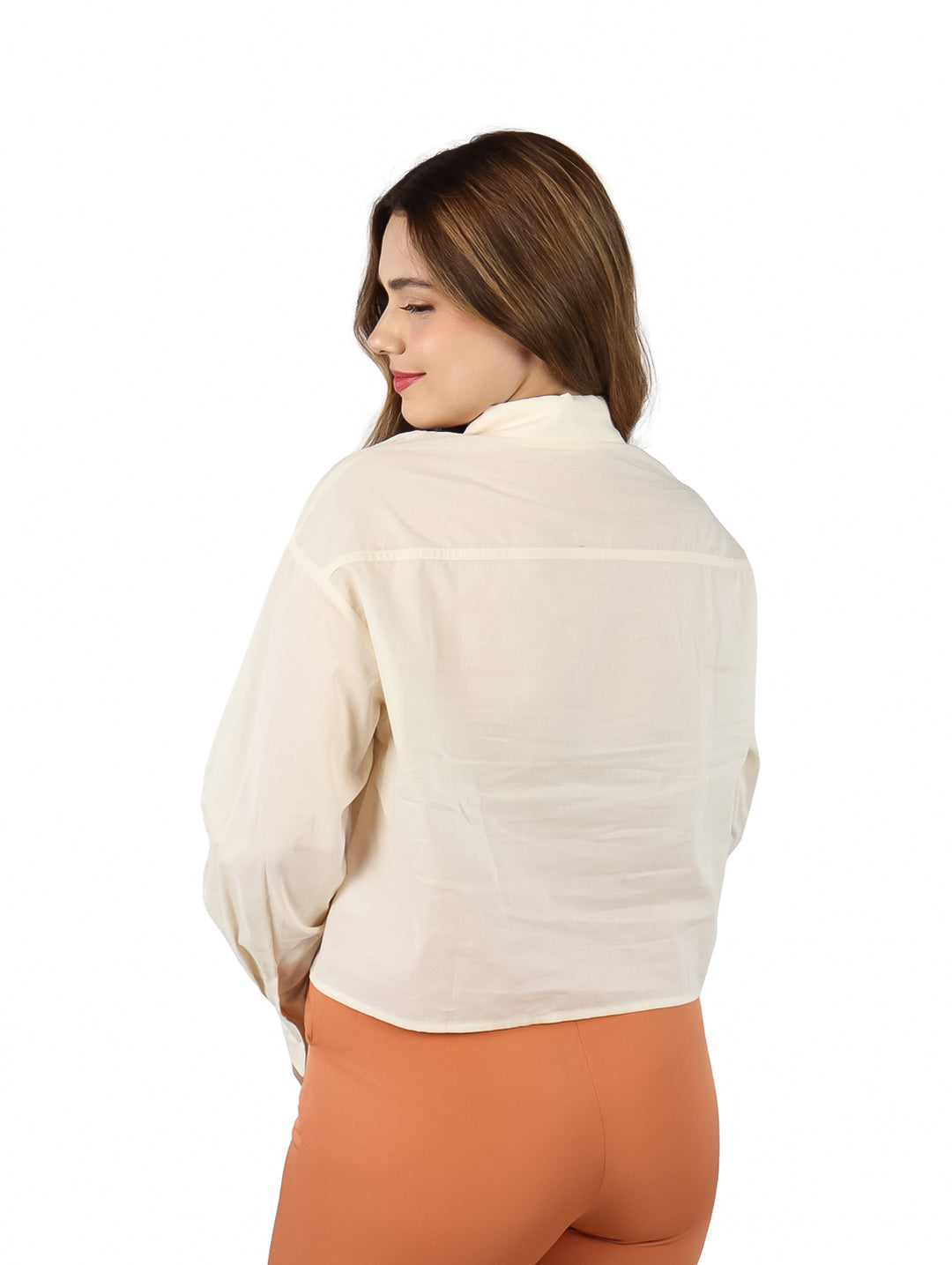 Mujer vistiendo una camisa color ivory de manga larga y pantalones naranja.