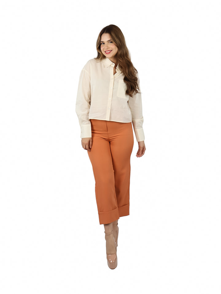 Mujer vistiendo una camisa color ivory de manga larga y pantalones naranja.